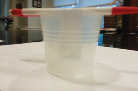 A clear, plastic cup with a pencil laying across the opening with a paper tag with half inch and 2 inch measurements