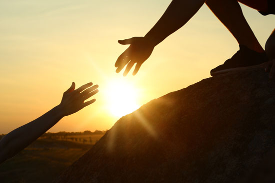 A picture of two hands reaching out towards each other, with the sun shining behind them