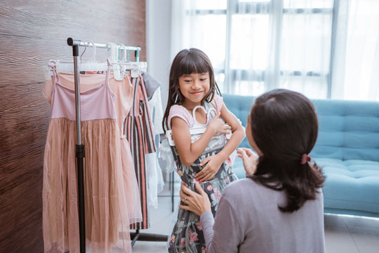 A child and their parent choosing a dress from a clothing rack