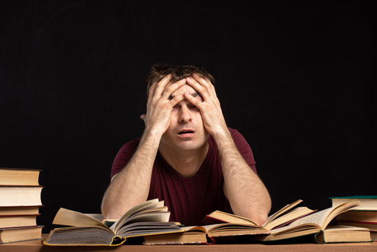 A person with their head in their hands surrounded by books on a desk