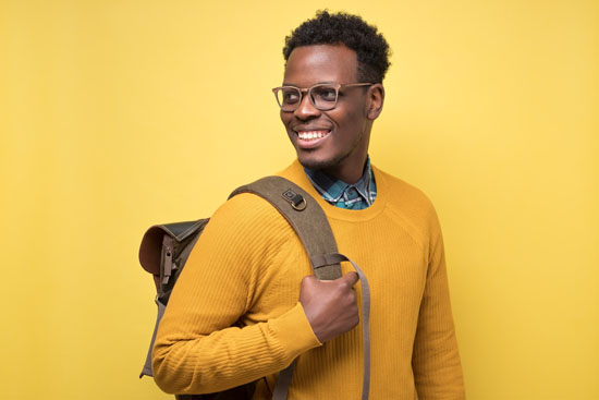 A student with a backpack, smiling and looking past their shoulder