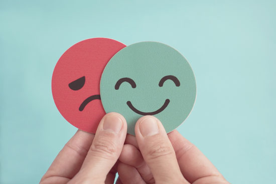 Hands holding a smiley face and a sad face
