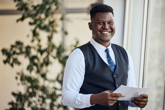 A smiling person, dressed for an office job, holding some papers