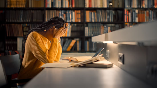 A person holds their head while leaning on a desk