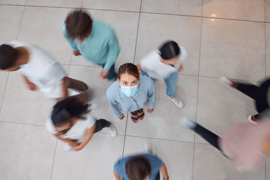 A person with a mask on, looking up while other people pass