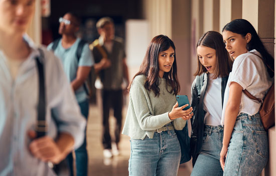 A group of students looking at a phone in shock, while one of them stares at another student