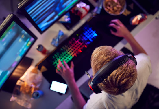 A person sitting in front of multiple computer screens with drinks and snacks all around
