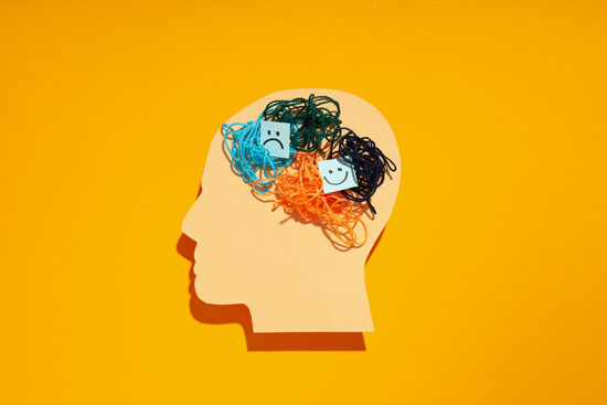 A paper cutout of a head with balls of yarn and happy and sad faces in the brain to represent bipolar disorder