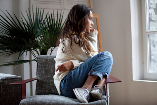 A person, curled up and concerned, looking out the window