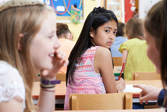 A young student, looking behind their shoulder to see two students whispering to each other