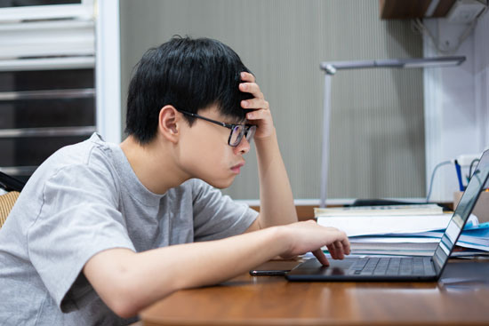 A picture of a student sitting at a desk and studying with a hand on their head