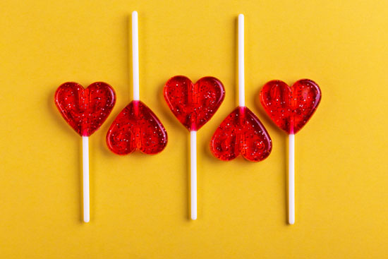 An image of five red, heart-shaped lollipops arranged in alternating directions