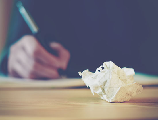 A crumpled piece of paper is in focus, with a person still writing in the background