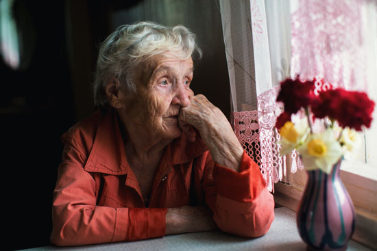 An older person looks sadly out the window