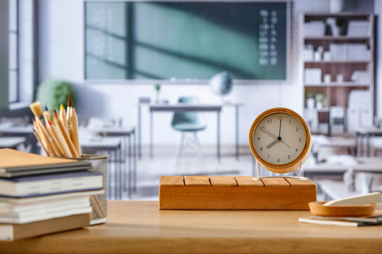 A desk topped with books, pencils, and a small clock