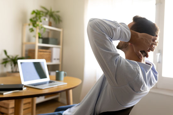 A person leaning back in their chair, hands behind their back