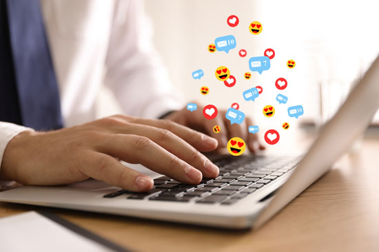 A person typing on their laptop, with images of reaction icons and notifications rising from the keyboard